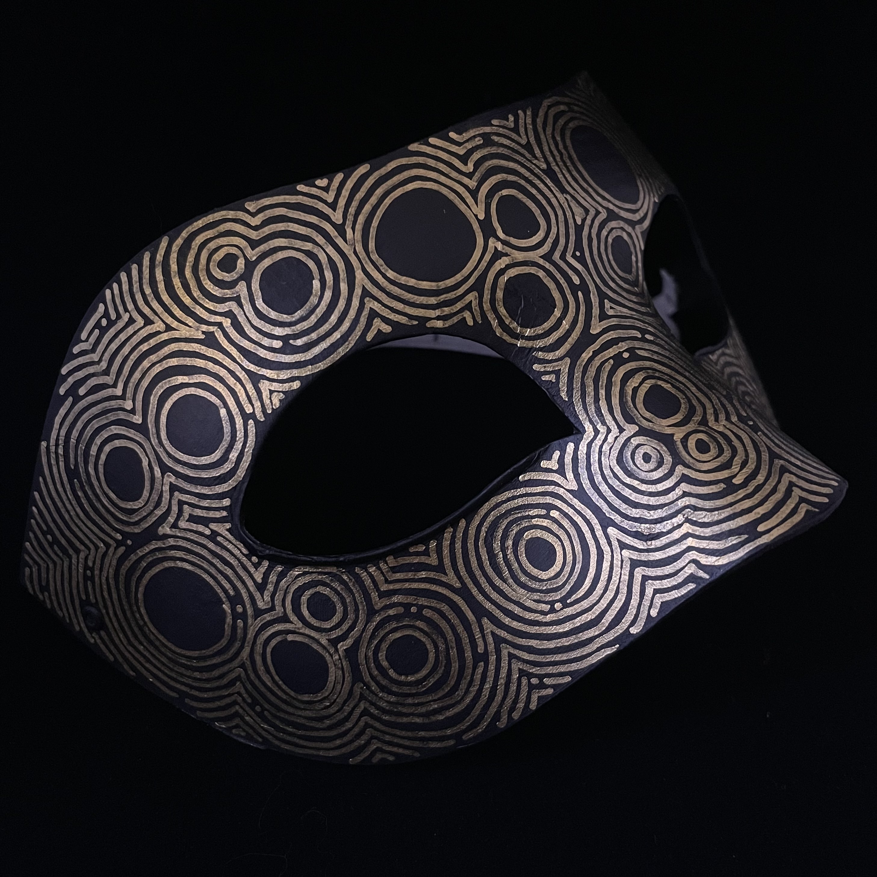 black mask with a gold circular pattern