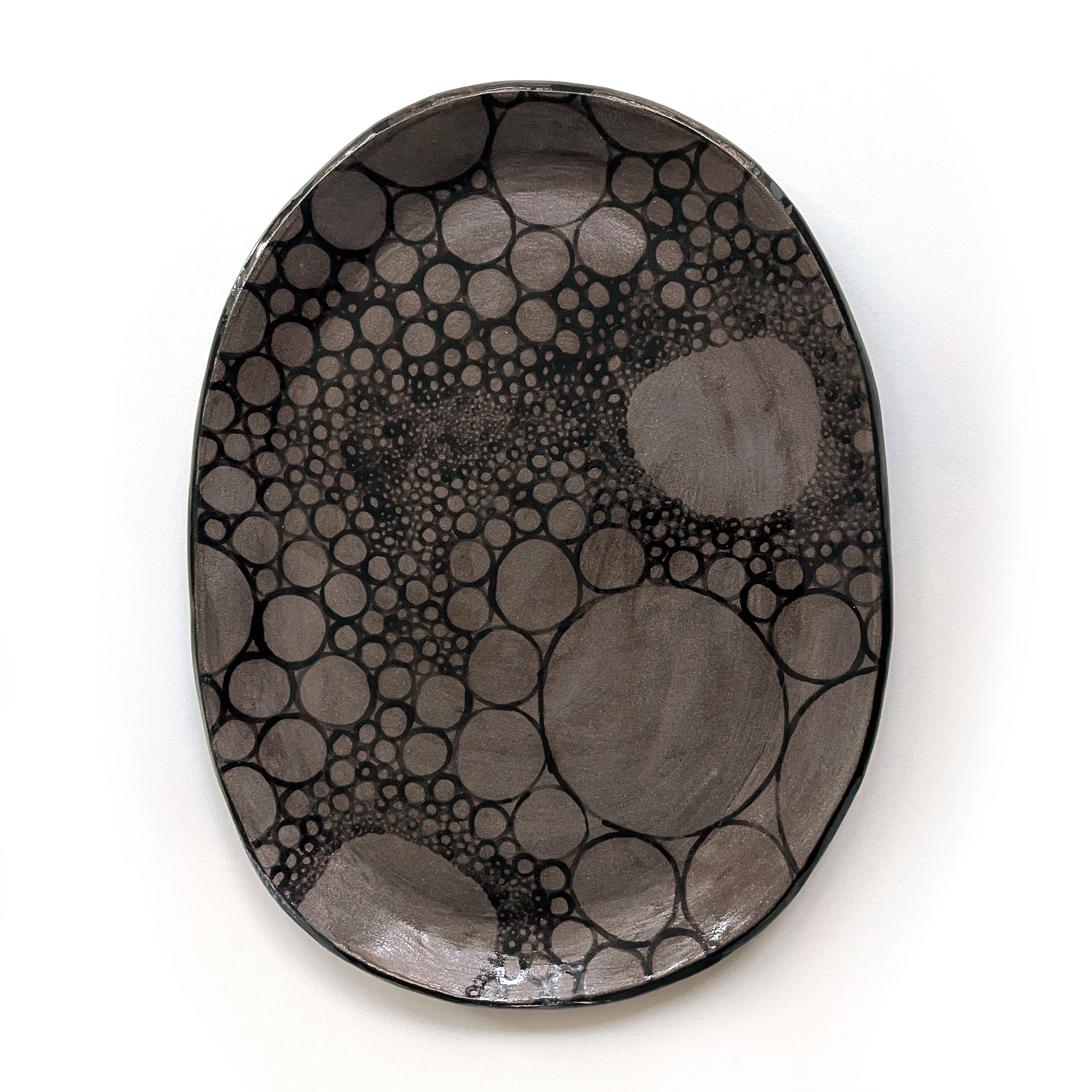 a dark grey ceramic plate with bubble-like patterns glazed in black