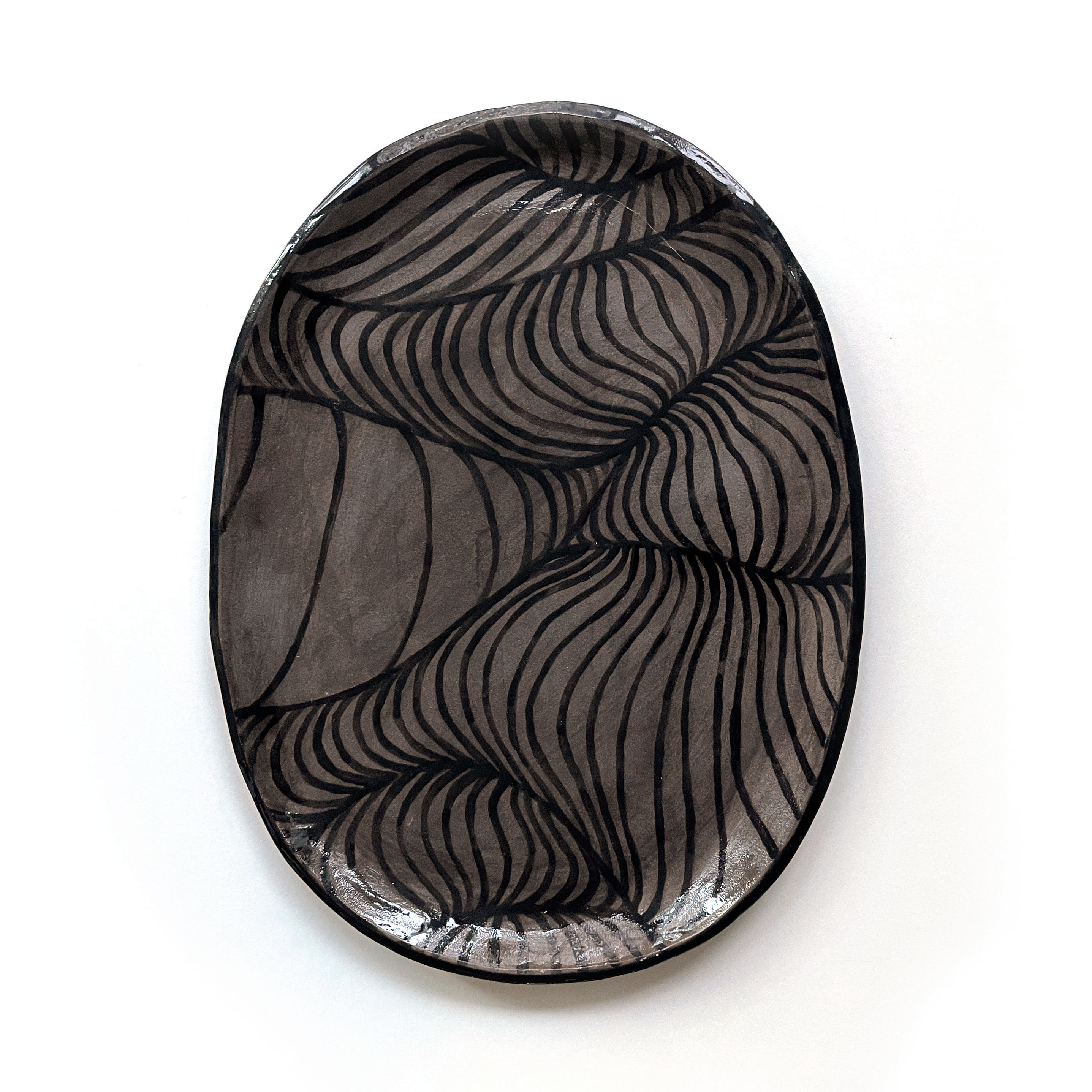 a dark grey ceramic plate with wave-like patterns glazed in black